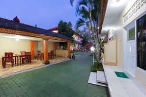A courtyard with a tiled floor, outdoor seating area with chairs and tables, and a building with a red-tiled roof.