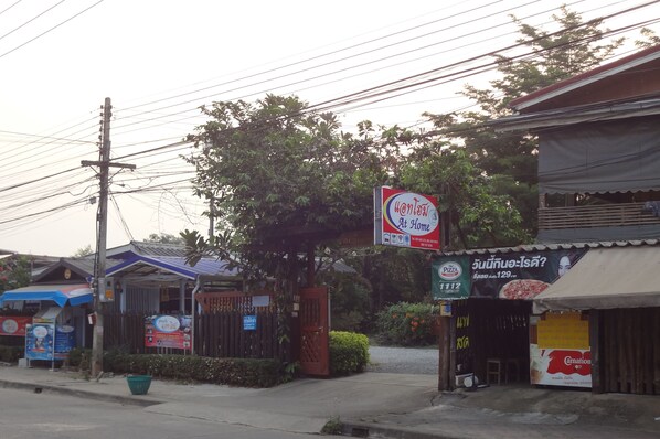 A street view with a sign for a home delivery service, a pizza shop, and a small storefront. - At Home Sukhothai (Sukhothai)