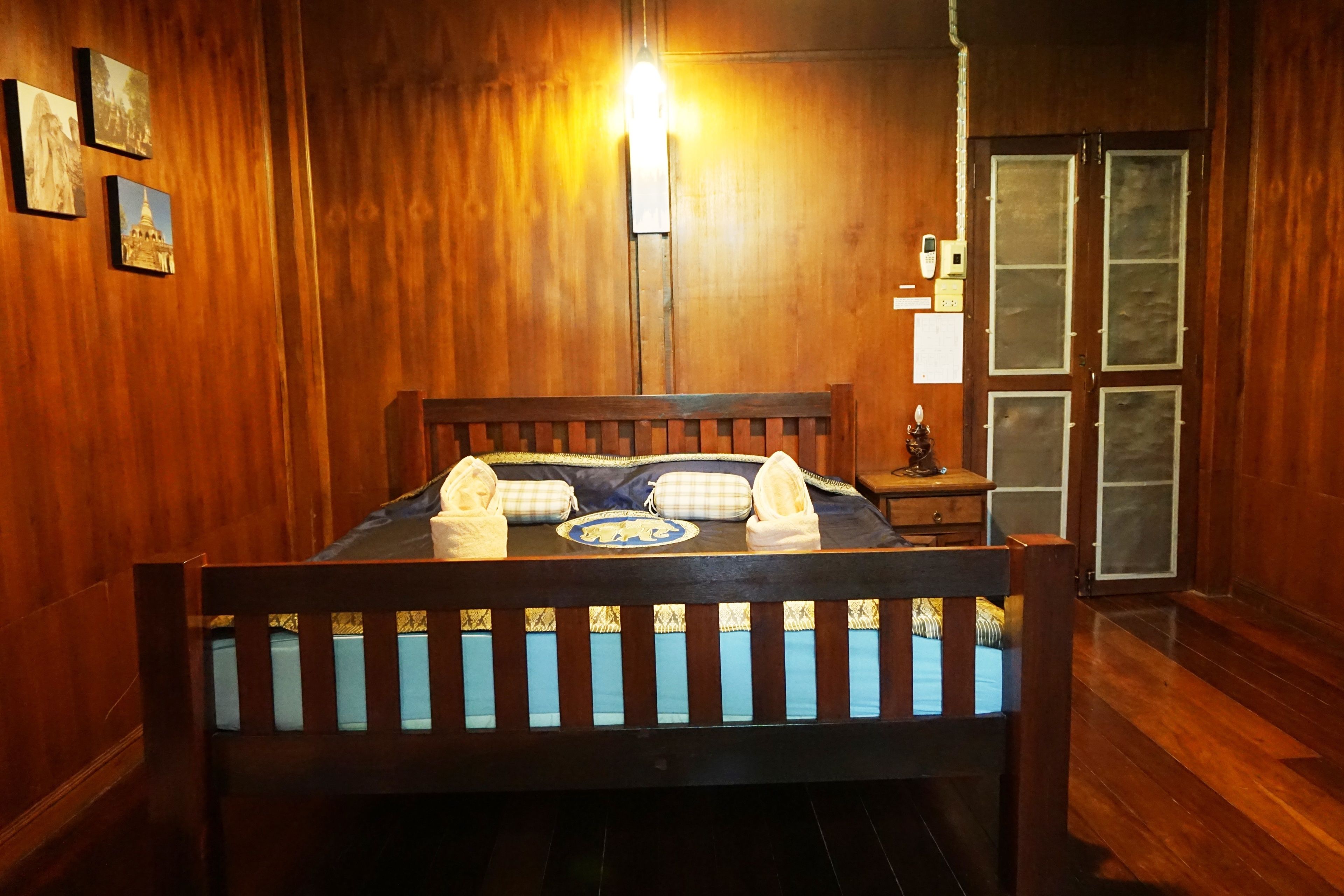 A wooden-framed bed with a blue and white checkered bedspread, a bedside table with a lamp, and a wooden door with frosted glass panels.