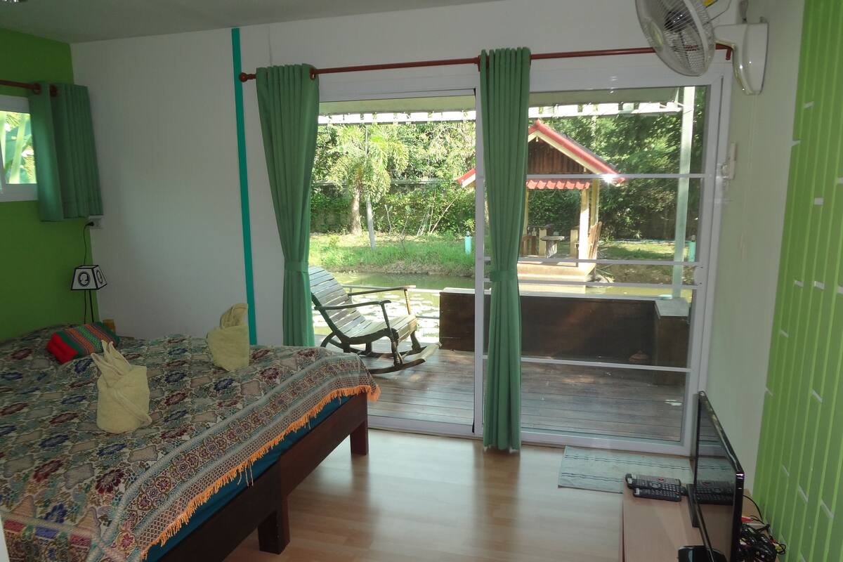 A bedroom with a bed, a rocking chair, a fan, and a view of the outdoors.