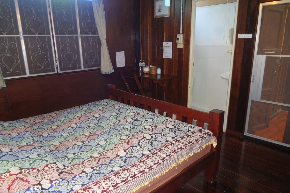 A room with a wooden bed, a small table with a basket and bottles, and a door with a sign.