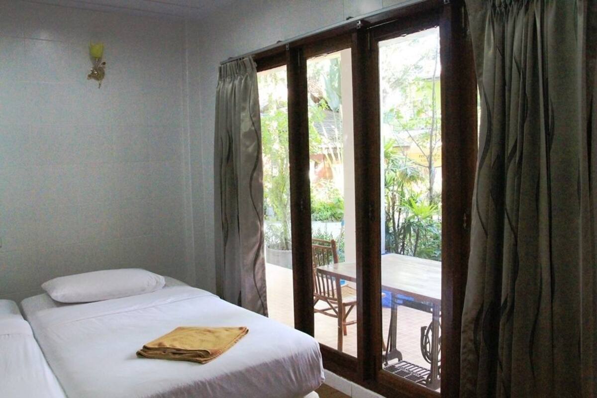A room with two beds, a window with curtains, and a view of an outdoor area with a table and chairs.