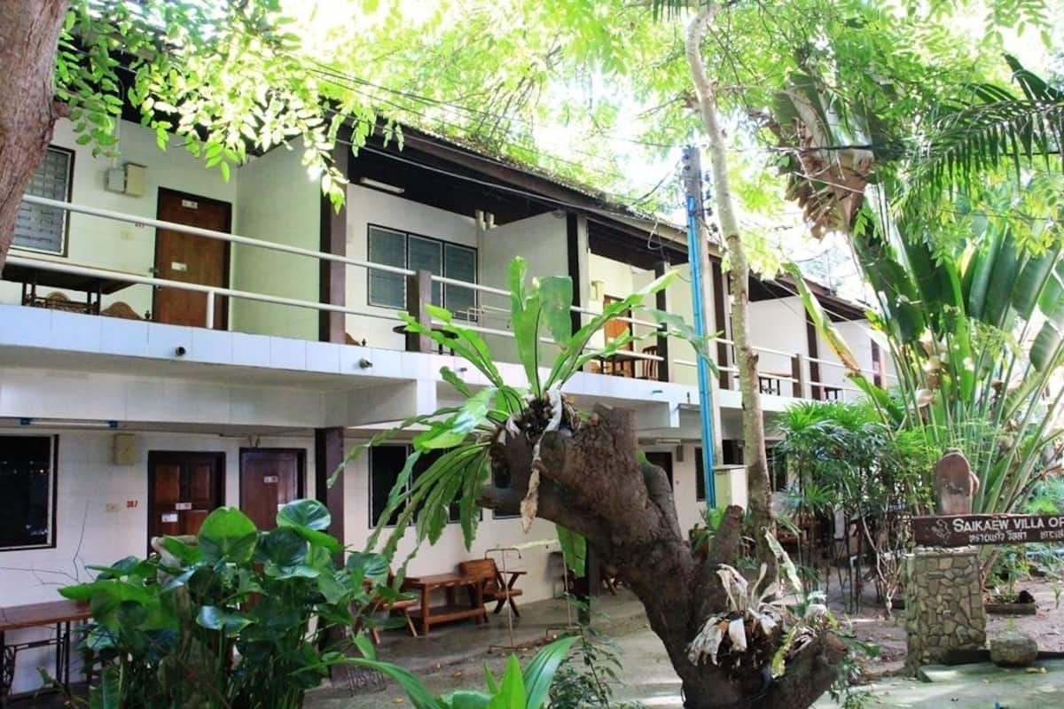 A two-story building with a balcony, surrounded by lush greenery and a sign reading "Saikaew Villa".