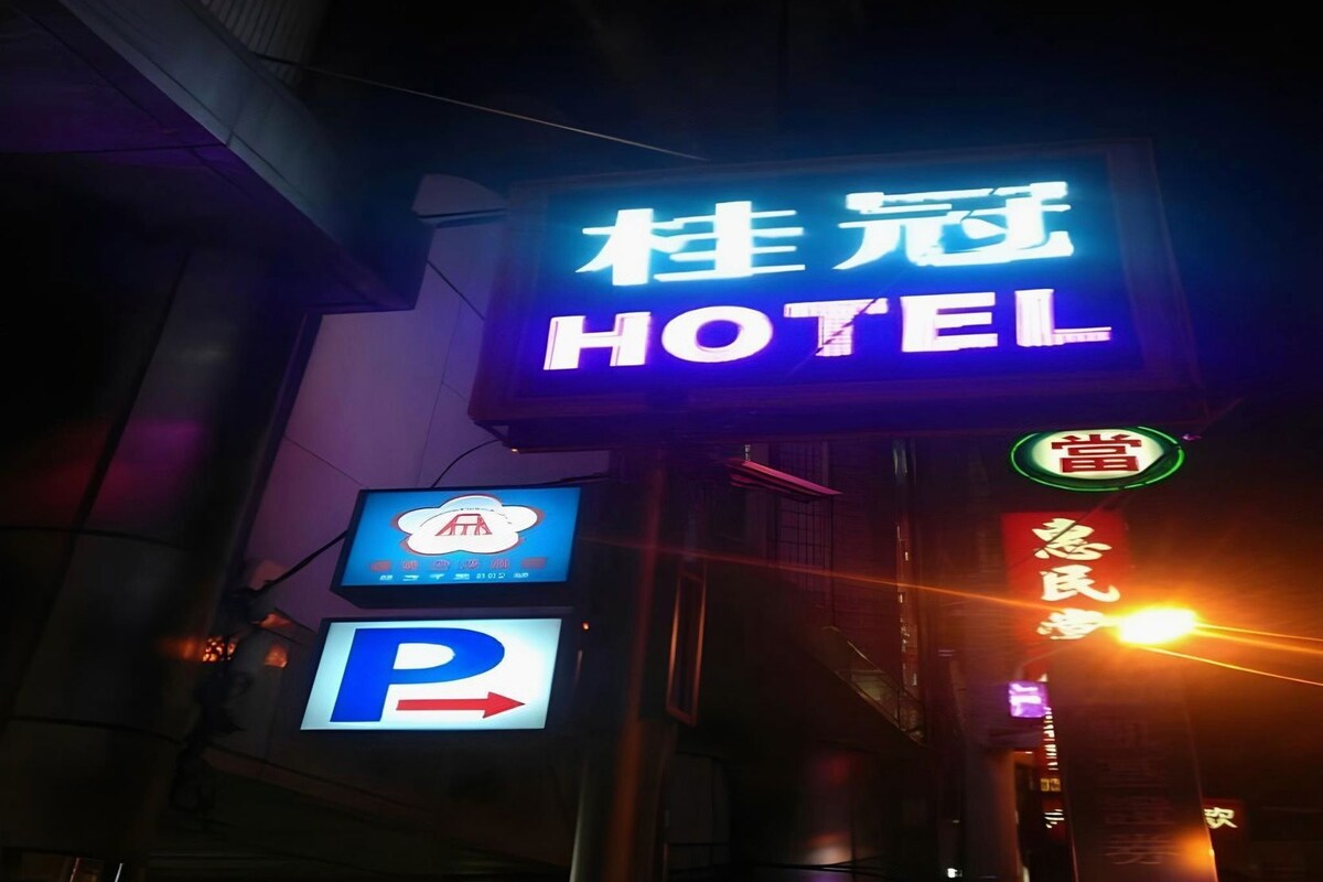 Ein Hotelschild mit einer leuchtenden Neonreklame mit dem Schriftzug 'HOTEL' und einem Hinweisschild für den Parkplatz darunter.