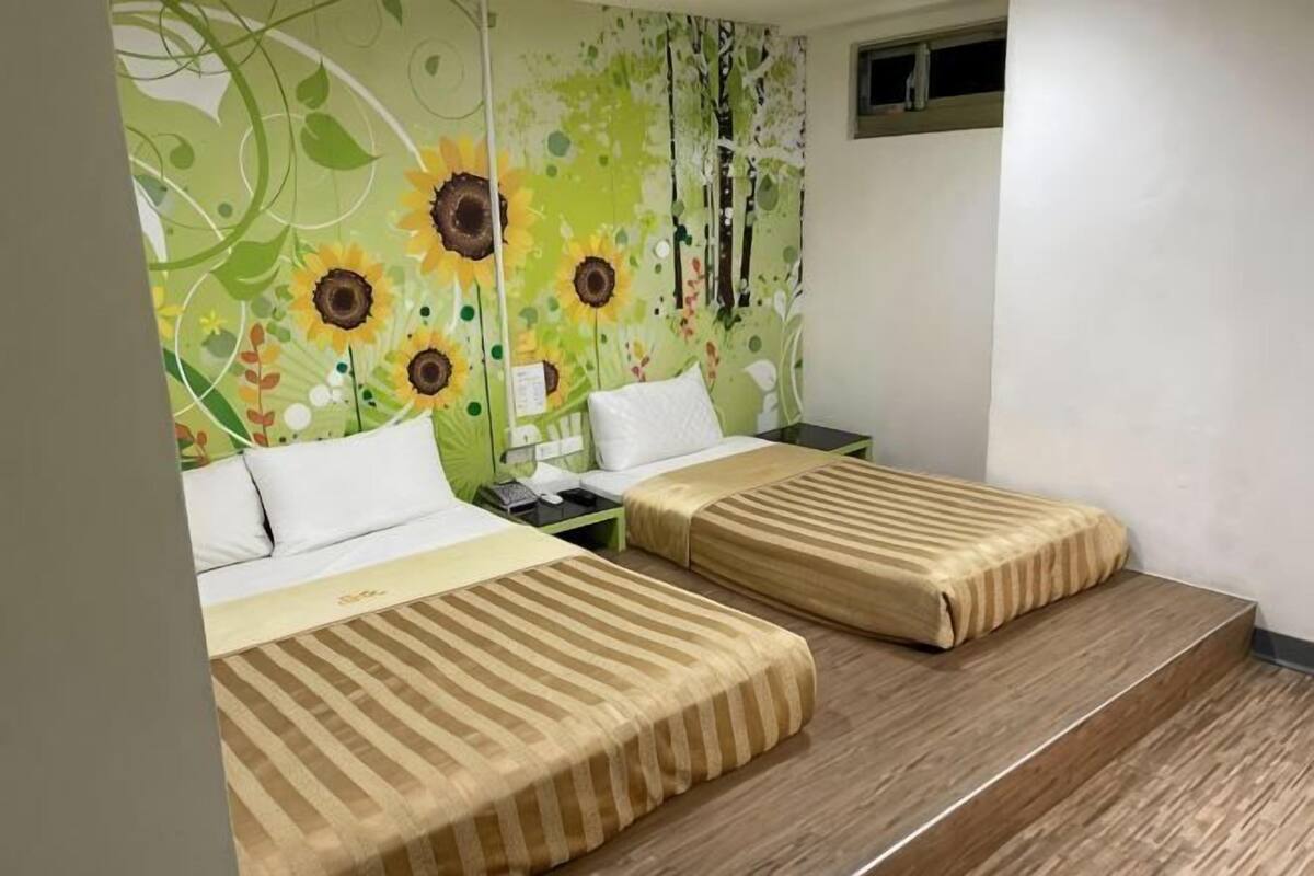 Une chambre avec deux lits, une table de chevet, un mur orné d’une fresque florale et une fenêtre.
