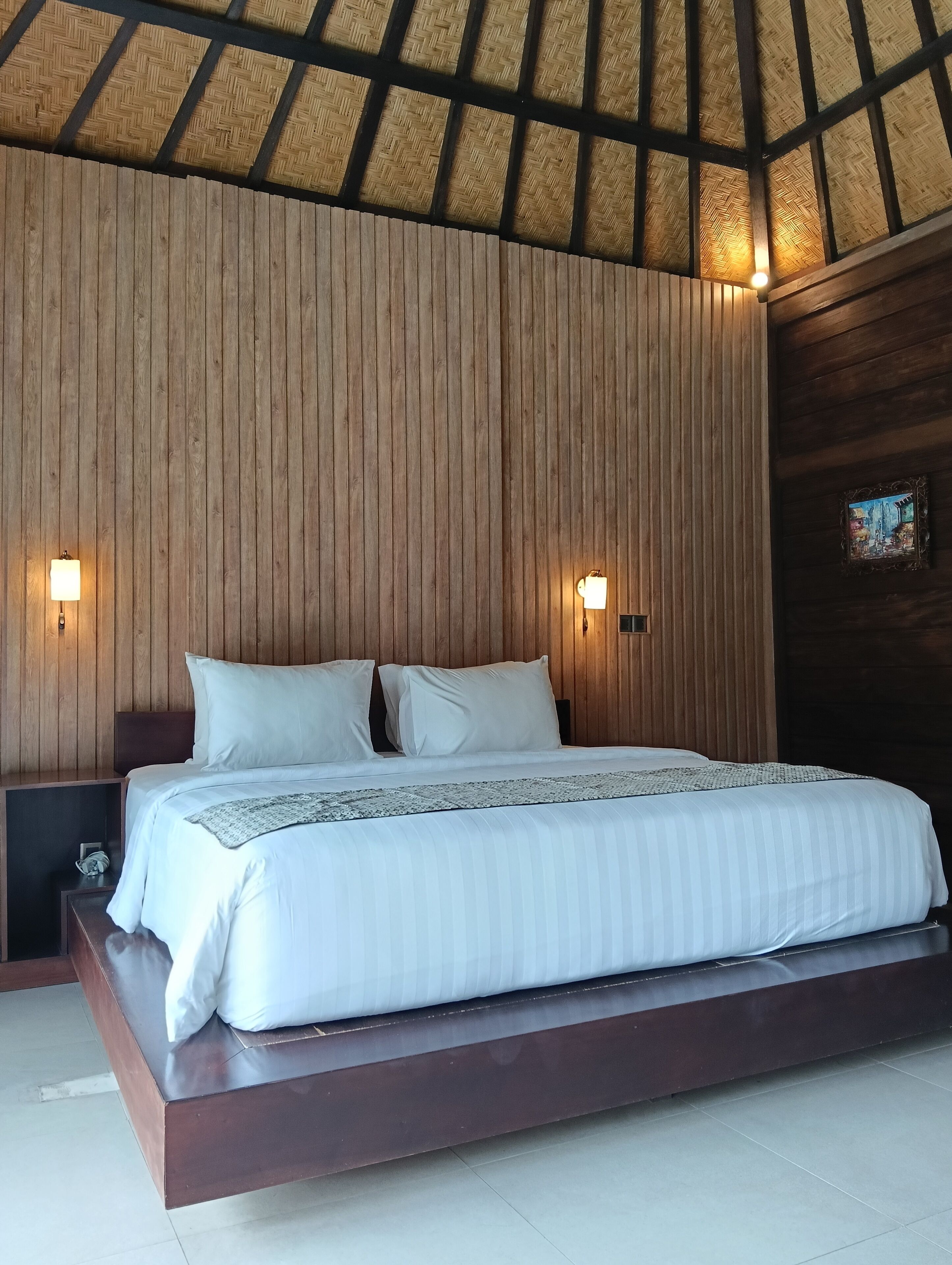 Una cama con cabecera de madera, dos lámparas de noche y una mesita con lámpara.