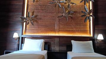 Habitación de hotel con dos camas, cabecera de madera con un panel decorativo y dos lámparas de noche.
