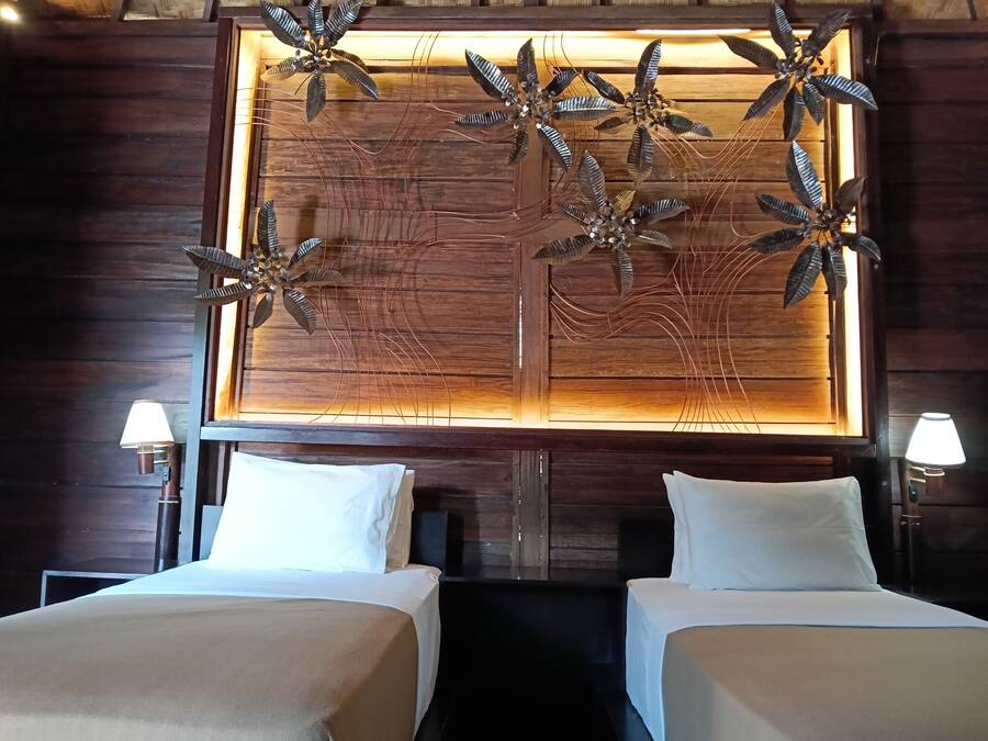 Habitación de hotel con dos camas, cabecera de madera con un panel decorativo y dos lámparas de noche.