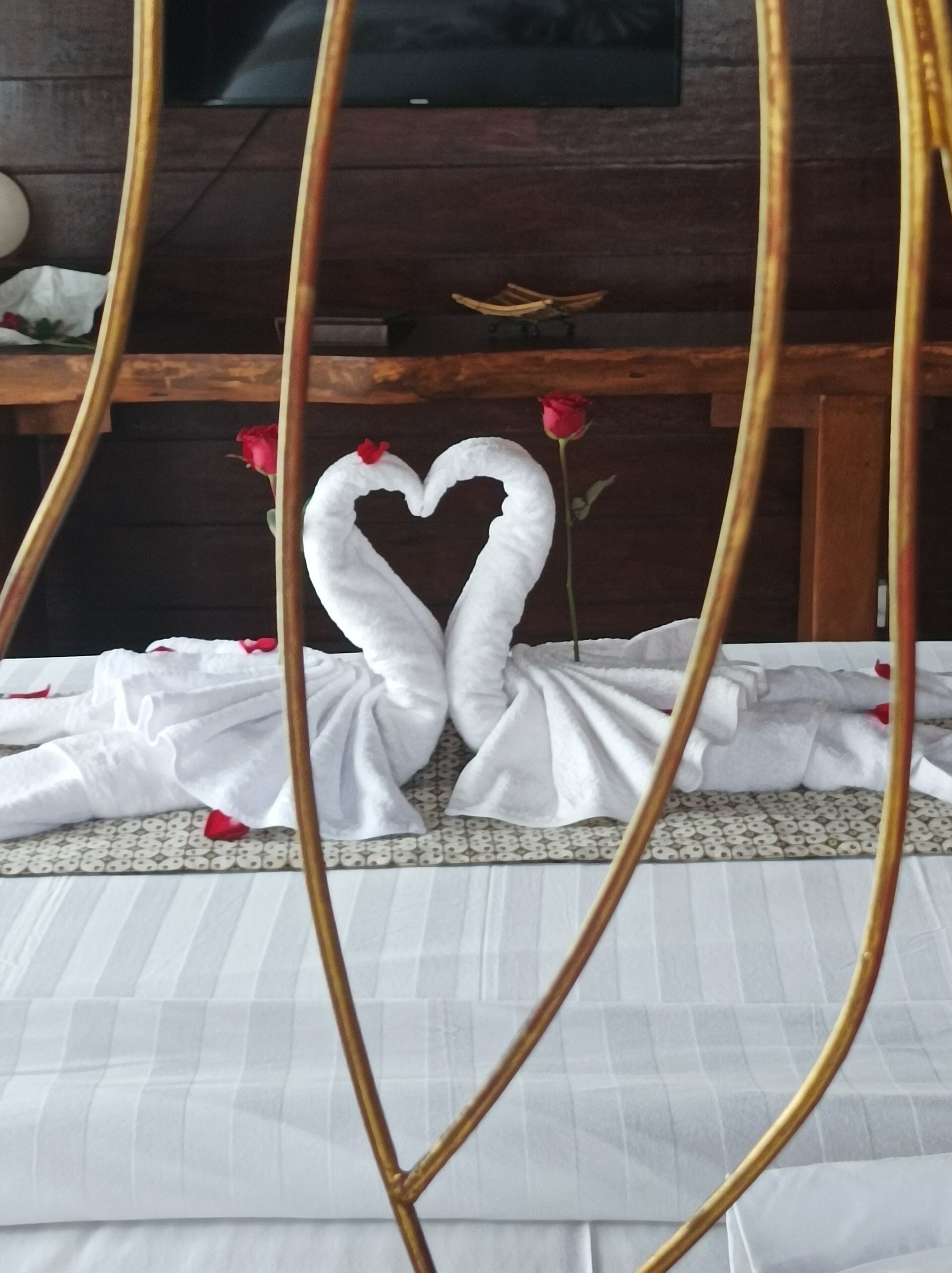 A bed with white linens and a heart-shaped towel arrangement.