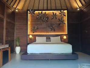A bedroom with a bed, two bedside lamps, a decorative wall panel, and a potted plant. - Sri Abi Ratu Villa (Penatih)