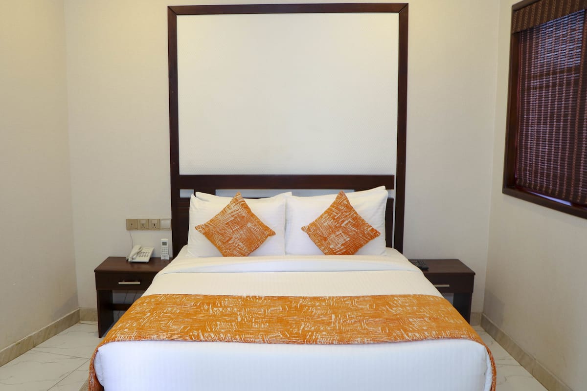 A neatly made bed with a white and orange bedspread, two pillows, and a wooden headboard.