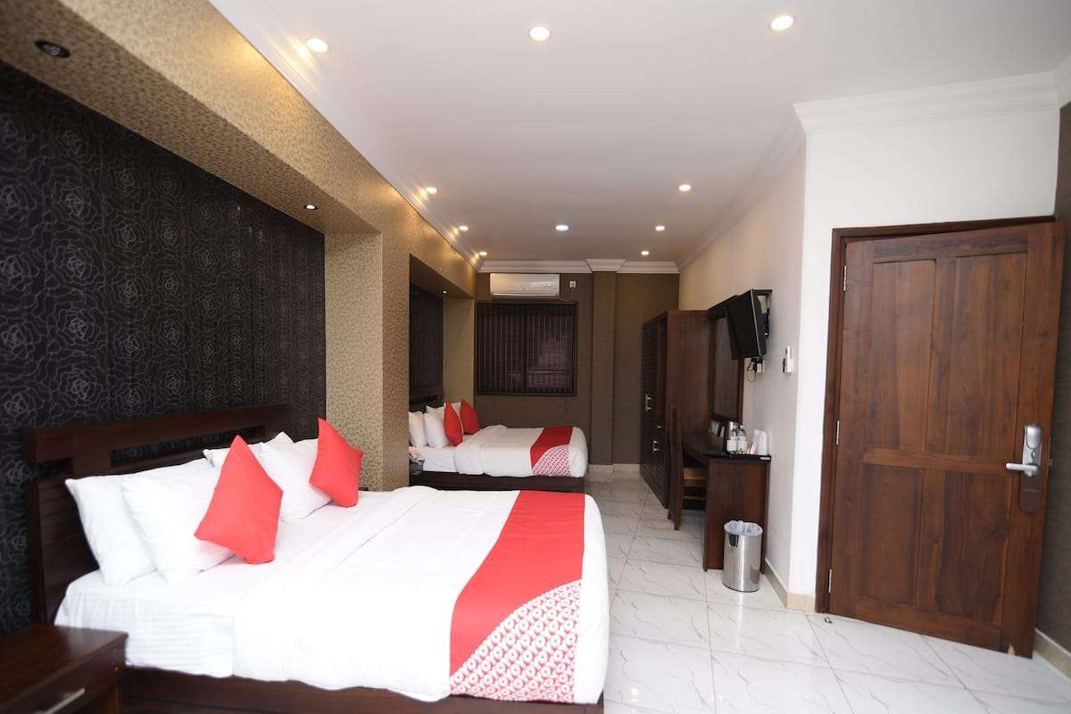 A hotel room with two beds, a wooden wardrobe, a TV, and a trash bin.