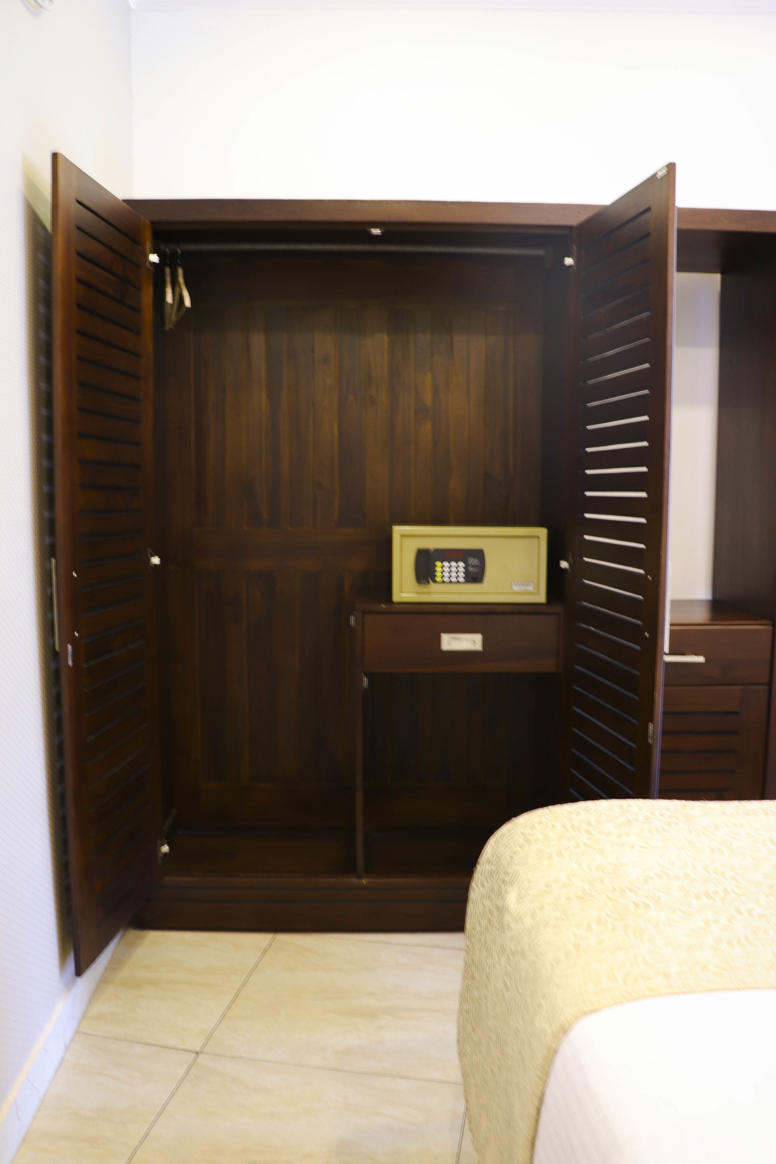 A room with a wooden wardrobe, a small desk with a radio, and a bed with a white bedspread.
