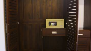 A room with a wooden wardrobe, a small desk with a radio, and a bed with a white bedspread.