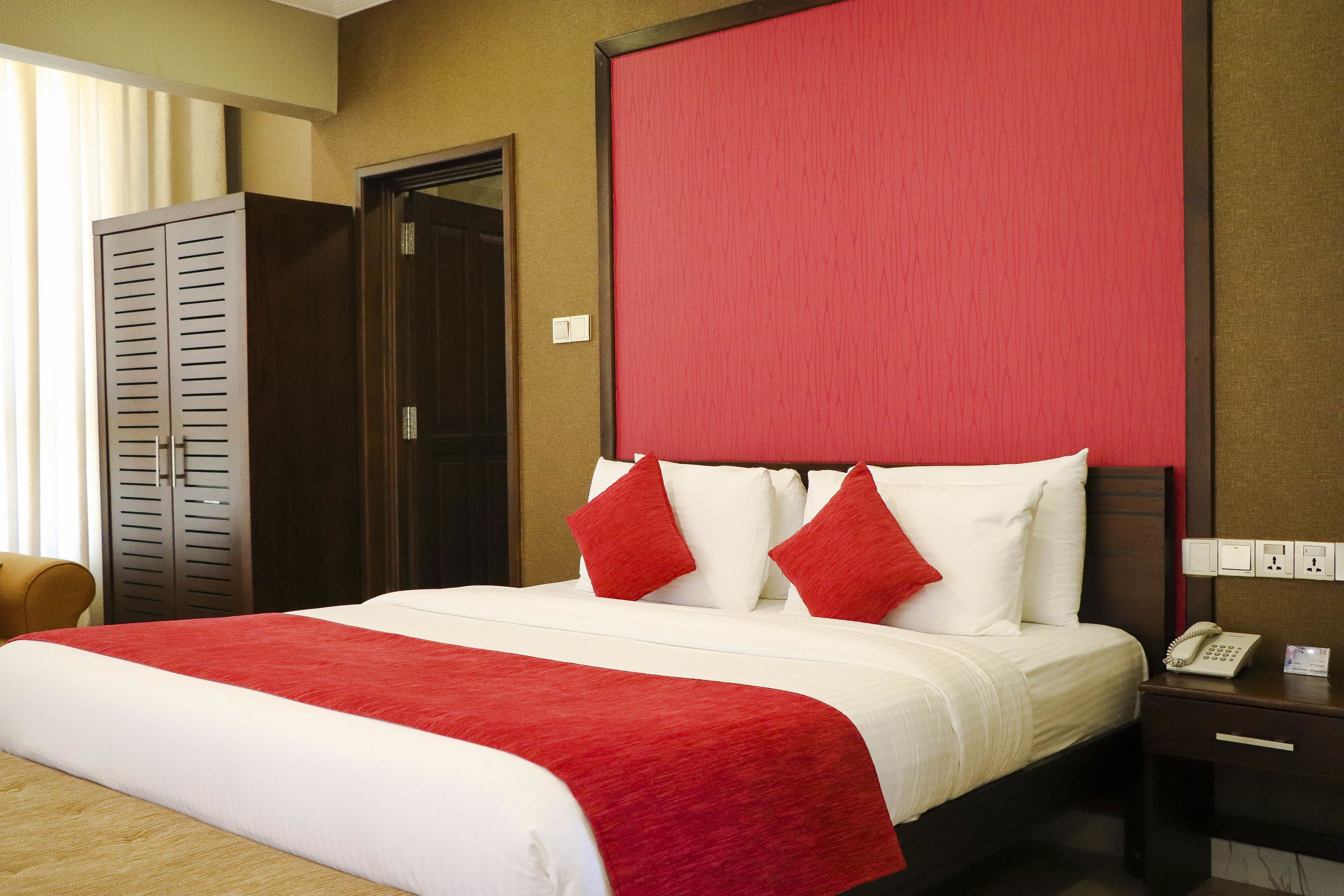 A hotel room with a large bed, a wooden wardrobe, a red headboard, and a bedside telephone.