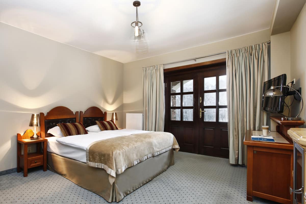 Una habitación de hotel con una cama grande, un cabecero de madera, un escritorio con una silla, una televisión y una ventana con cortinas.