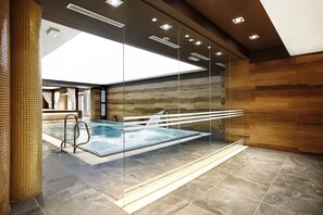 A modern indoor swimming pool with clear glass walls, a tiled floor, and a wooden wall. - Hotel Aubrecht Country SPA Resort (Przechlewo)