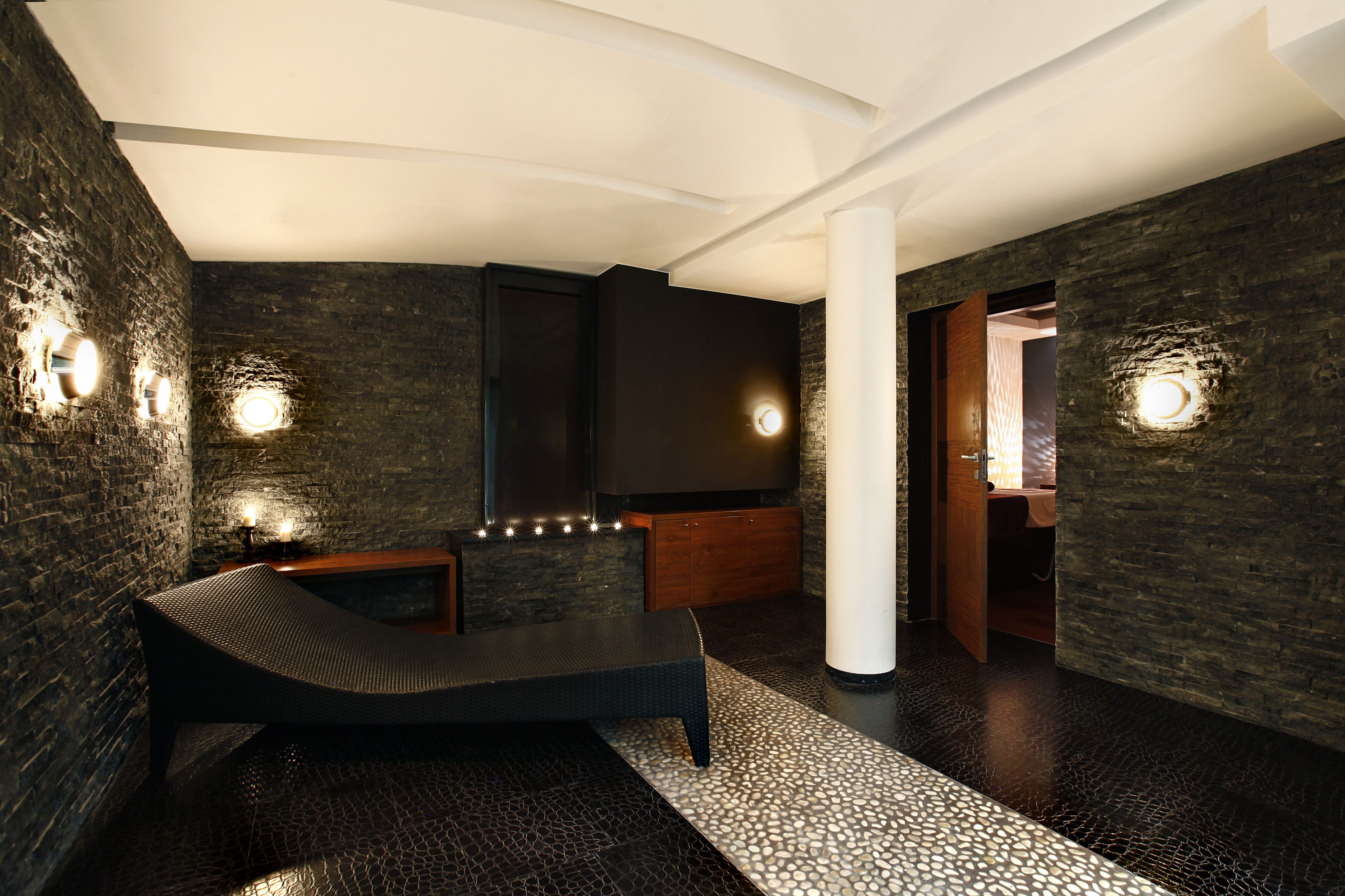 A modern spa room with a dark stone wall, a wooden bench, and a white pillar.