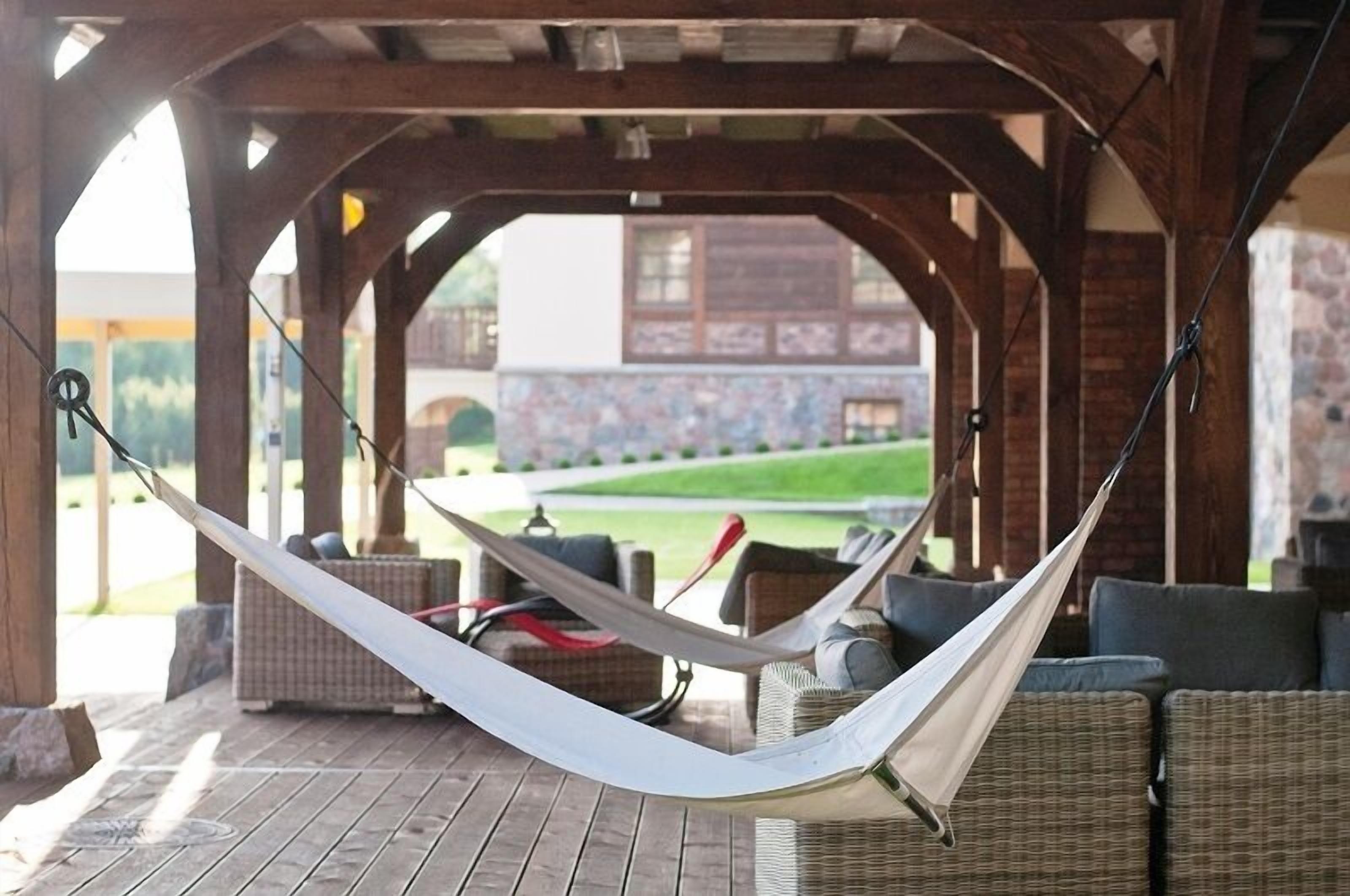 A hammock under a wooden pergola with wicker furniture and a view of a stone building.