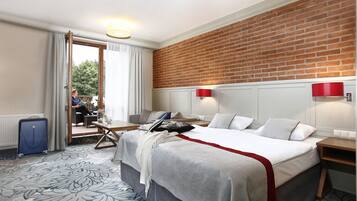 Een hotelkamer met een groot bed, een bureau, een stoel, een koffer en uitzicht op de omgeving door een schuifdeur.