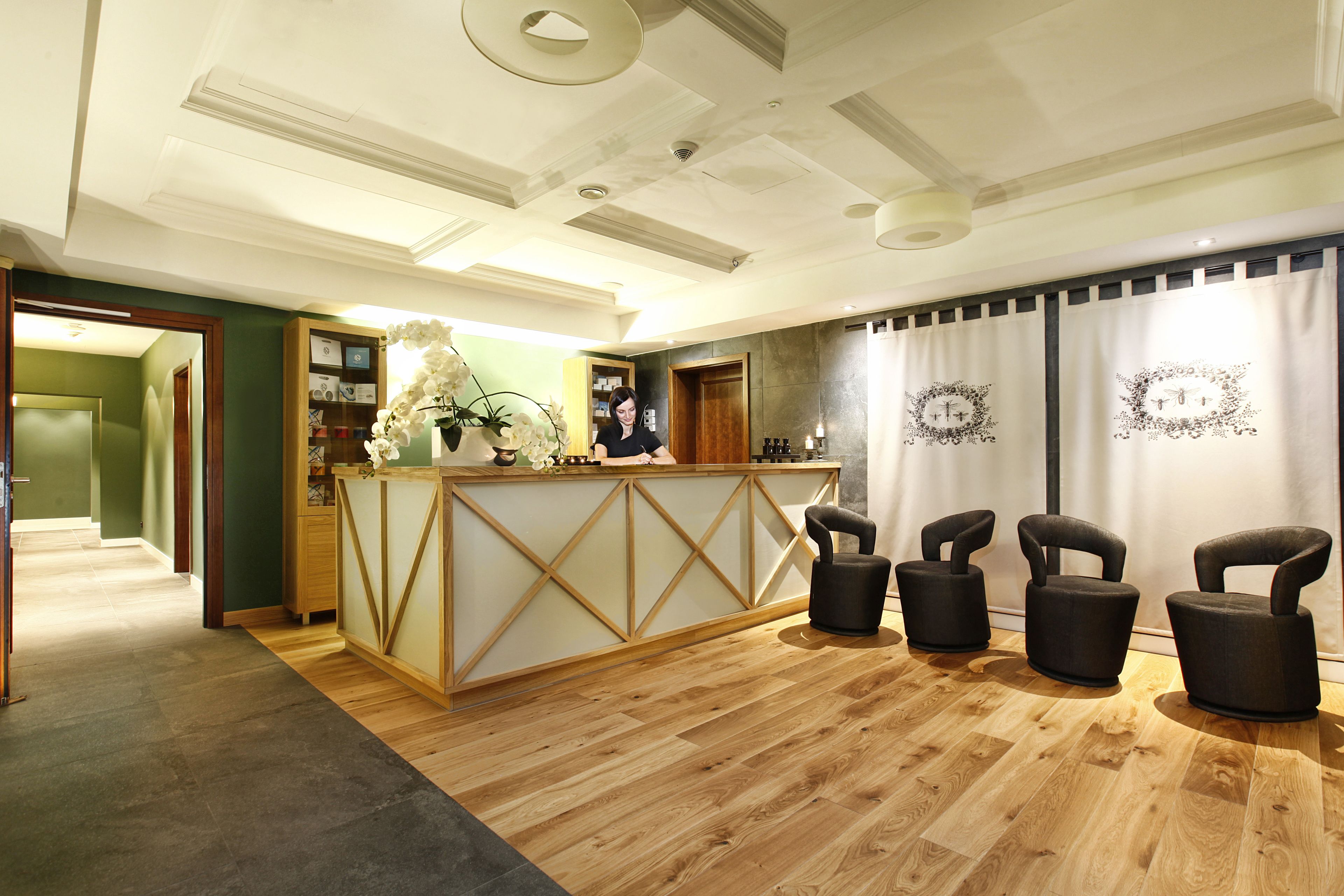 A reception area with a wooden reception desk, three black chairs, a potted plant, and a wall with framed pictures.