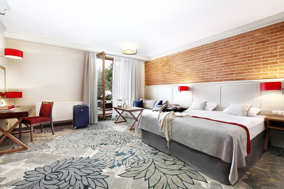 Habitación de hotel con cama, escritorio, silla, maleta y vista al exterior.