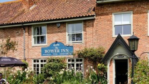 Ein traditionelles Backsteingebäude mit einem Schild, das 'The Bower Inn' ankündigt und einen Pub, ein Restaurant, Zimmer und eine Gartenterrasse anbietet.