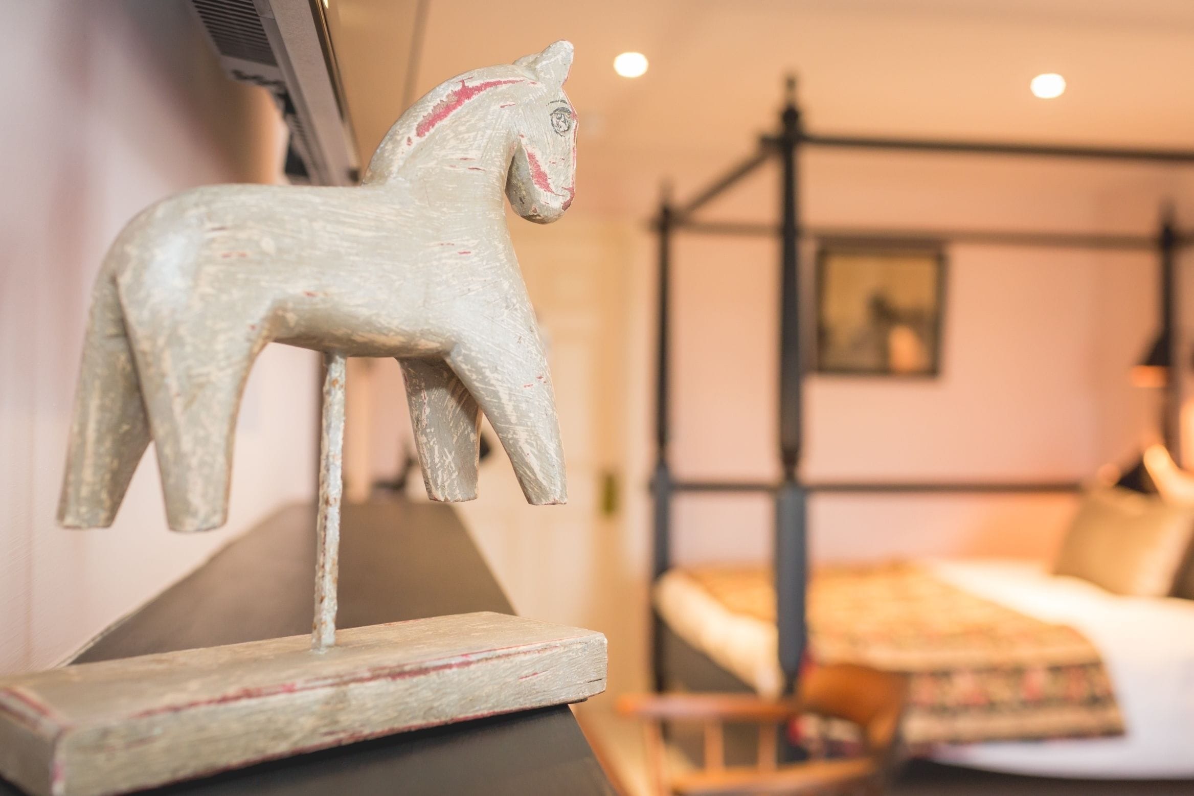Una escultura rústica de madera con forma de caballo sobre un pedestal en una habitación con cama con dosel y una decoración sencilla y acogedora.