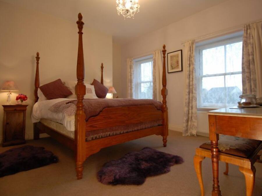 A four-poster bed with a wooden frame, a small bedside table with a lamp, and a window with curtains.