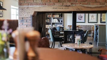 Un interior acogedor con una pared de ladrillo, una estantería y un comedor con sillas y mesas.