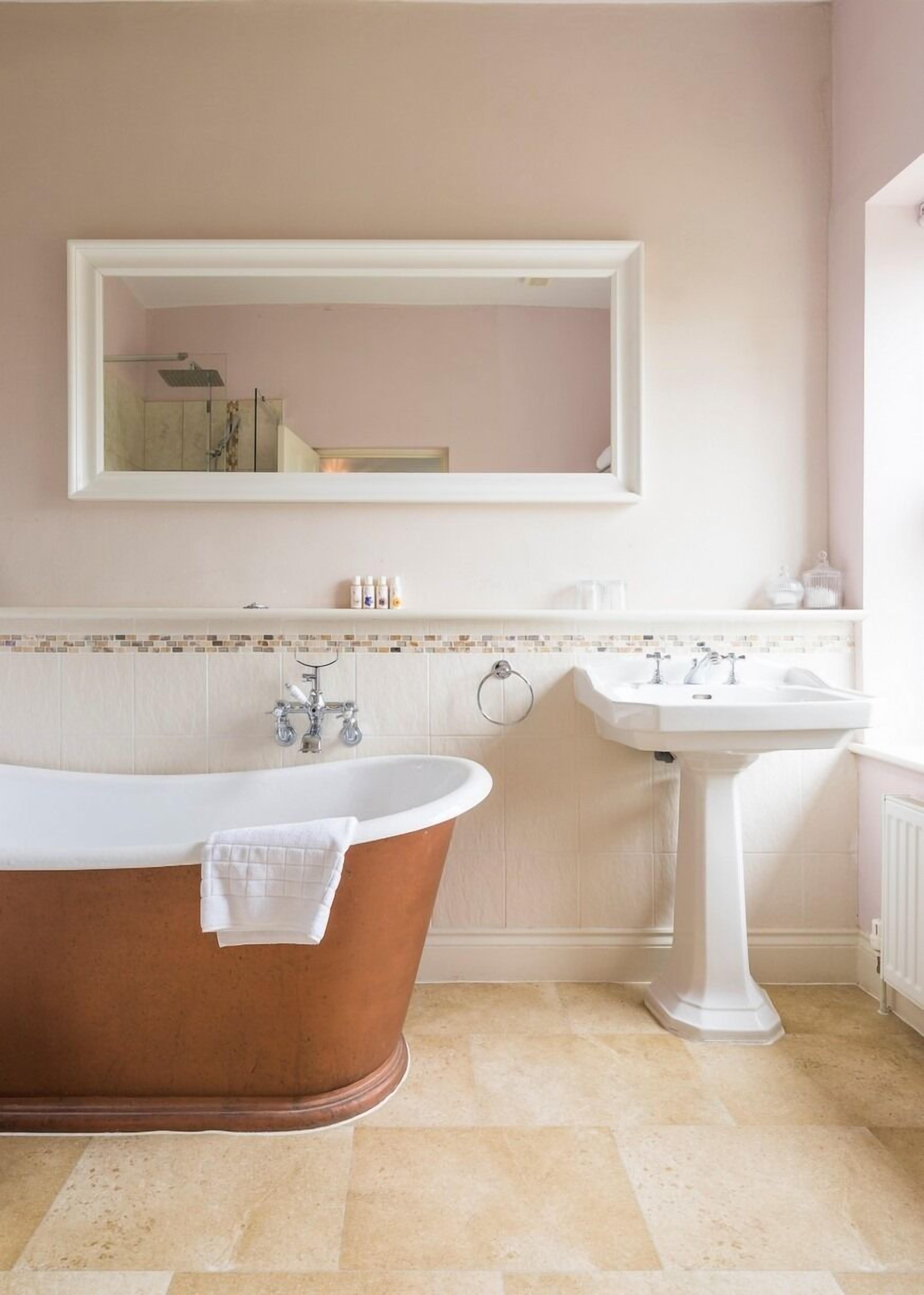 A bathroom with a freestanding bathtub, a pedestal sink, and a large mirror.