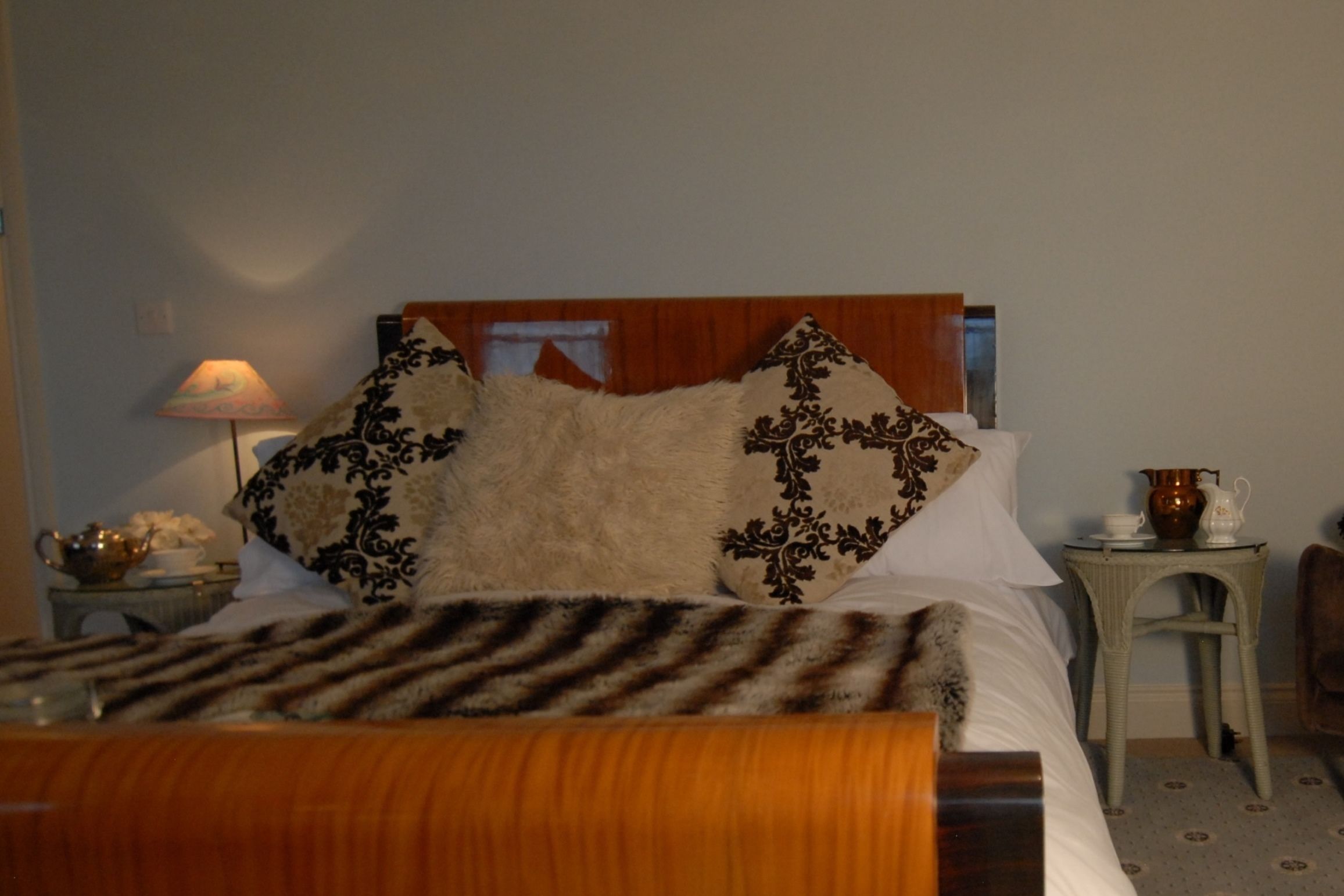 A bed with patterned pillows, a lamp, and a small table with a pitcher.