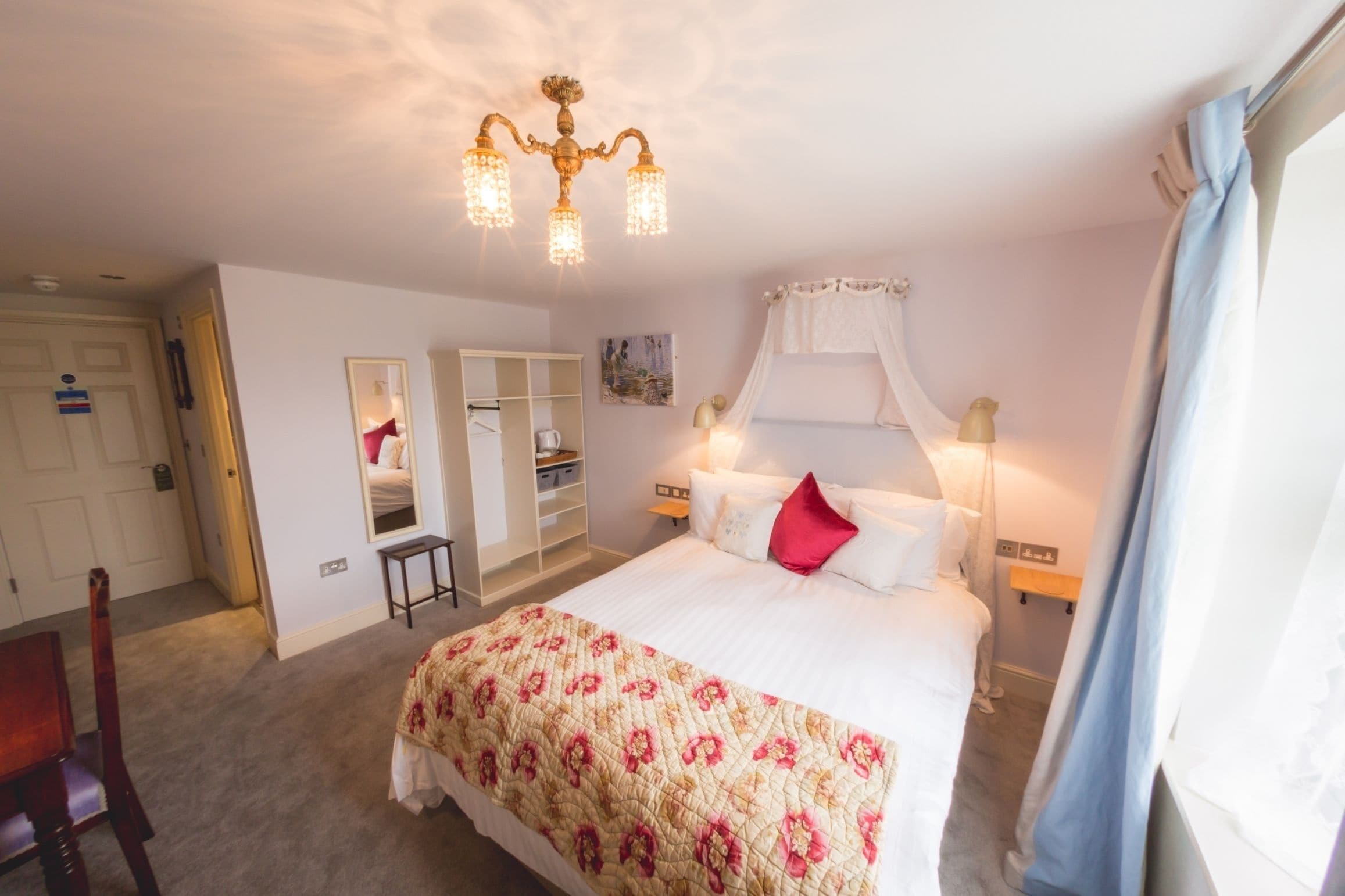 Een slaapkamer met een groot bed, een kroonluchter, een kledingkast en een spiegel.