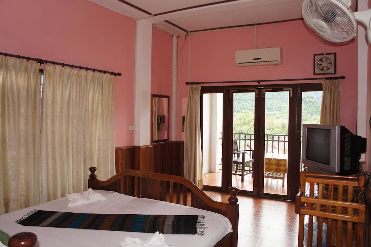 Une chambre d’hôtel comprenant un lit, un téléviseur posé sur un meuble en bois, un climatiseur et un balcon avec une table et des chaises.