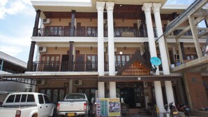A multi-story building with a balcony on the second floor, a signboard, and parked vehicles in front.