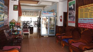 A waiting area with wooden furniture, a refrigerator, and a poster advertising bus and air ticket services.