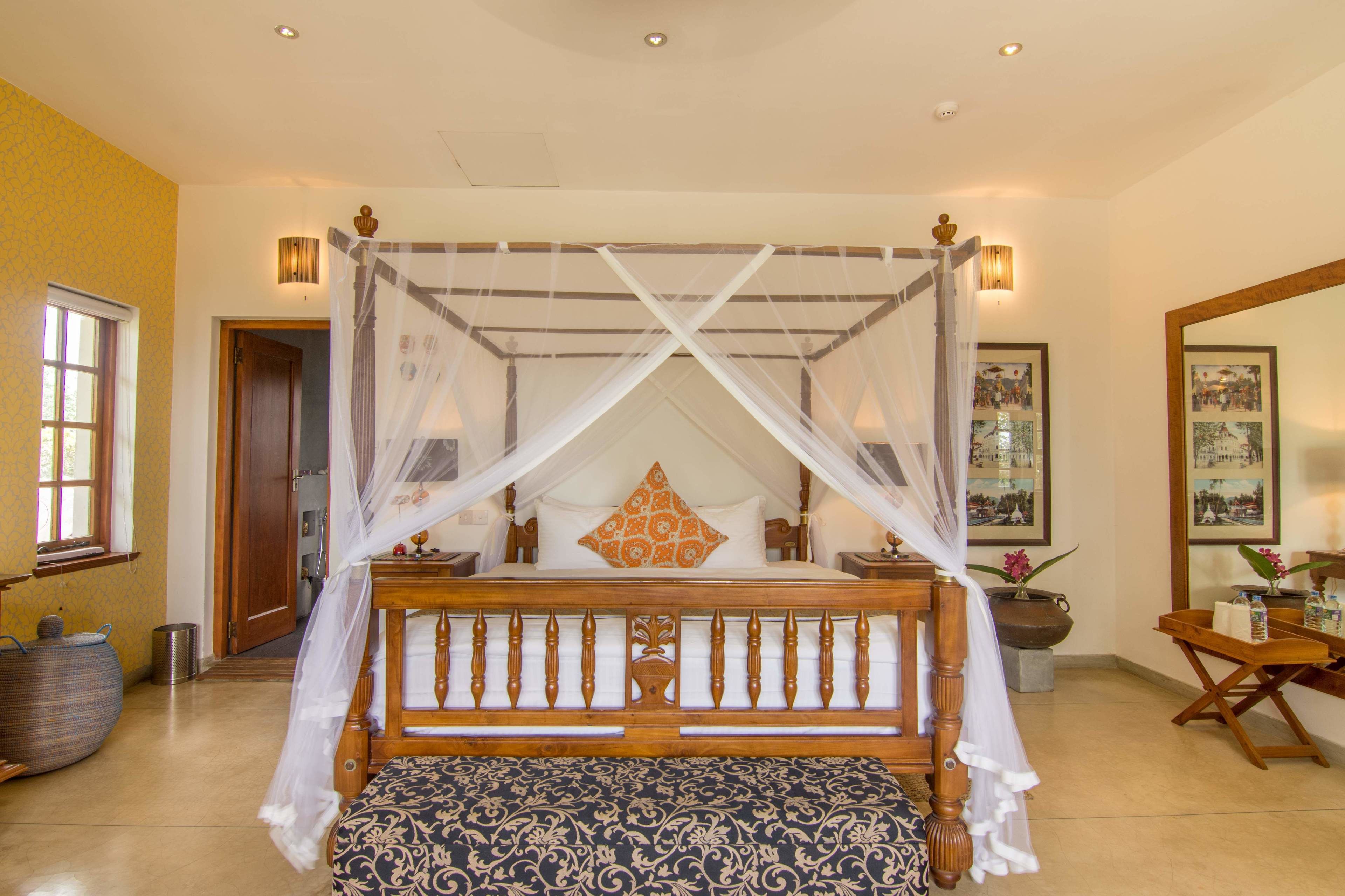 A four-poster bed with a canopy, a wooden bench, and a bedside table with a vase of flowers.