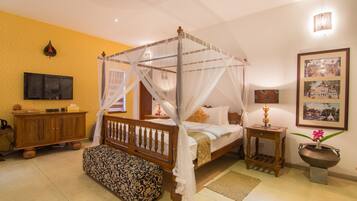 A four-poster bed with a canopy, a wooden bench, a bedside table with a lamp, and a wall-mounted TV.