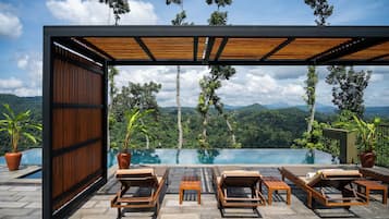 A modern outdoor pool area with wooden loungers and a view of a mountainous landscape.