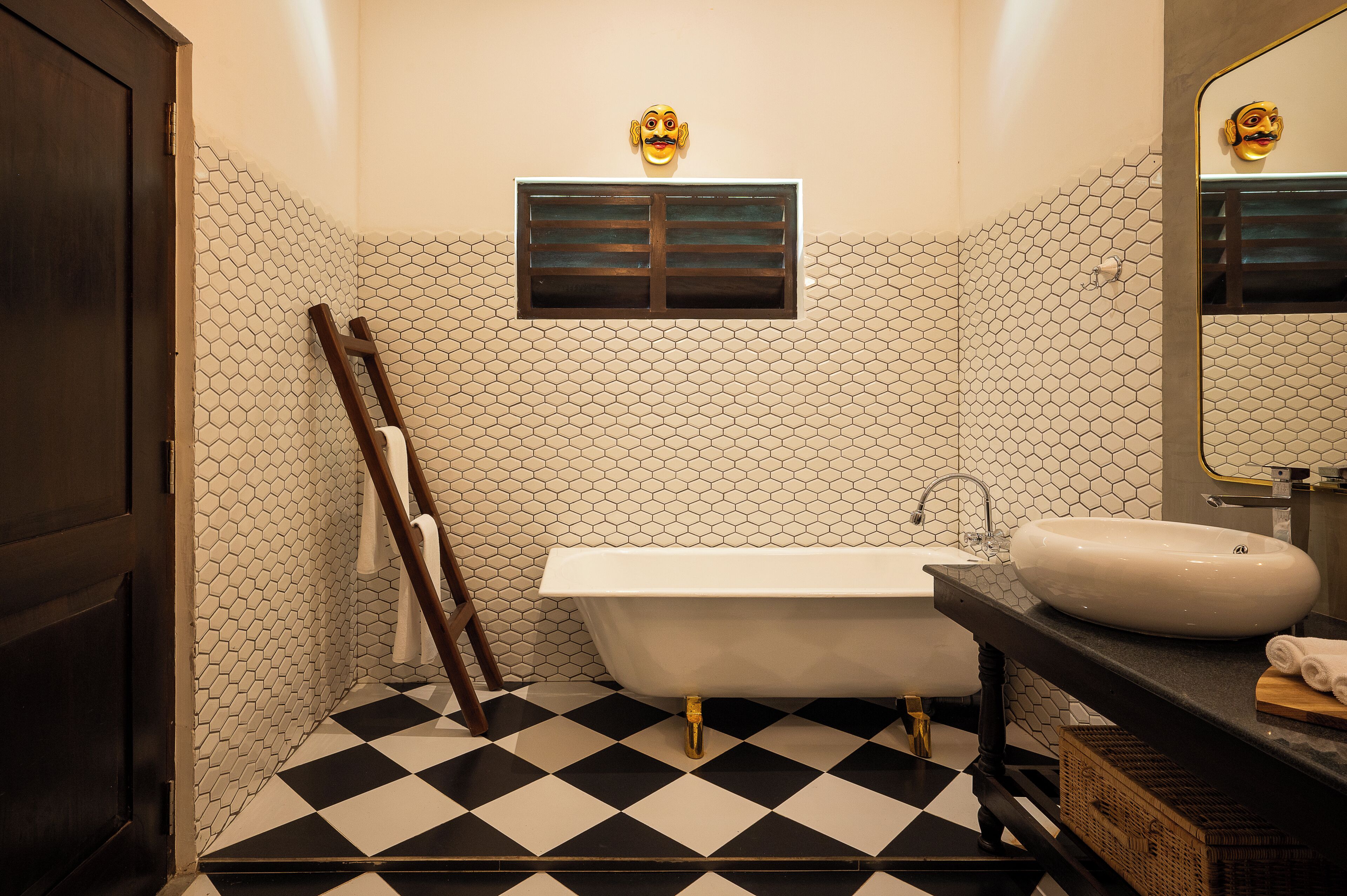 A bathroom with a black and white checkered floor, a white bathtub, a white sink, and a mirror with a gold frame.