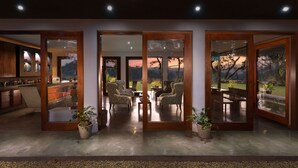 A spacious living area with a view of a sunset over mountains, large sliding glass doors, and a kitchen area with wooden cabinets and a radio. - The Elephant Stables (Kandy)