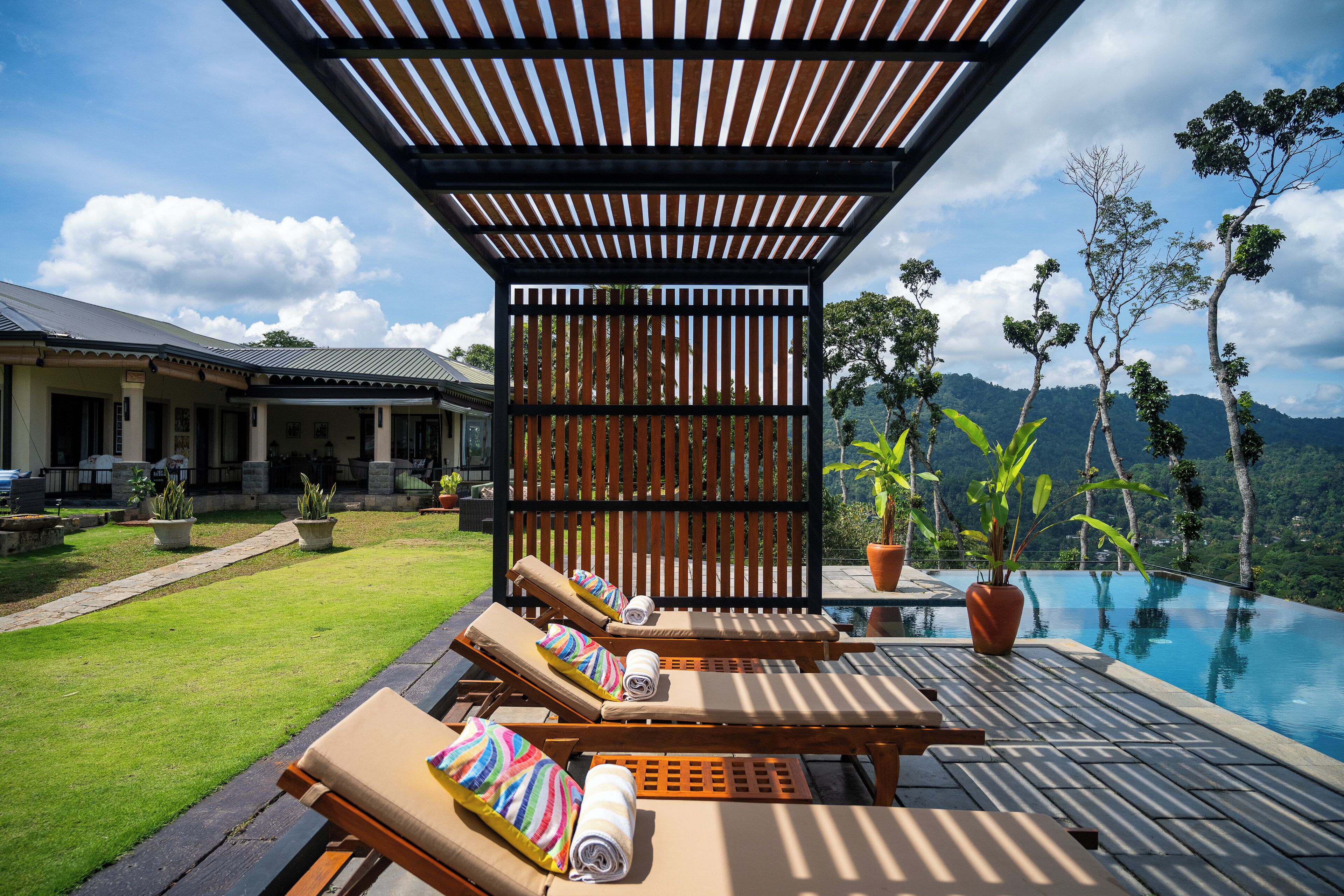 A poolside area with lounge chairs, a pergola, and a view of a mountain.