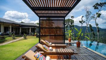 A poolside area with lounge chairs, a pergola, and a view of a mountain.