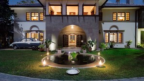 A two-story house with a central arched entrance, a driveway, and a circular water feature in the front yard. - The Elephant Stables (Kandy)