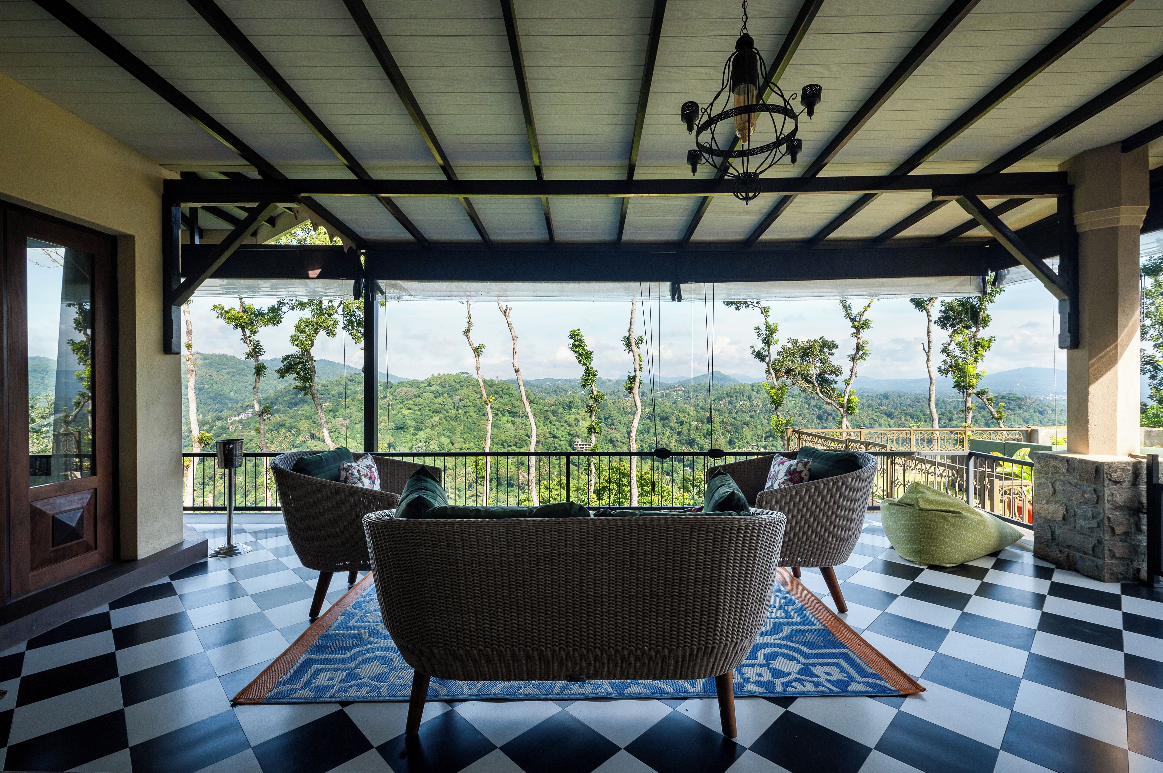 A covered balcony with checkered flooring, wicker furniture, and a view of a mountainous landscape.