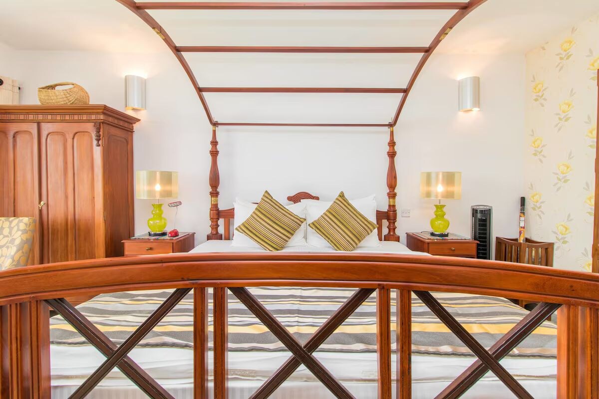 A bedroom with a four-poster bed, wooden furniture, and wall-mounted lamps.