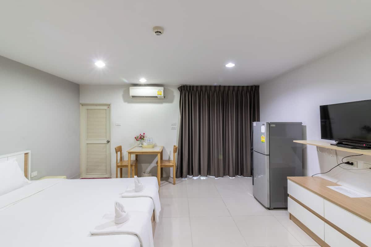 A hotel room with a bed, a desk with a chair, a refrigerator, a television, and an air conditioning unit.