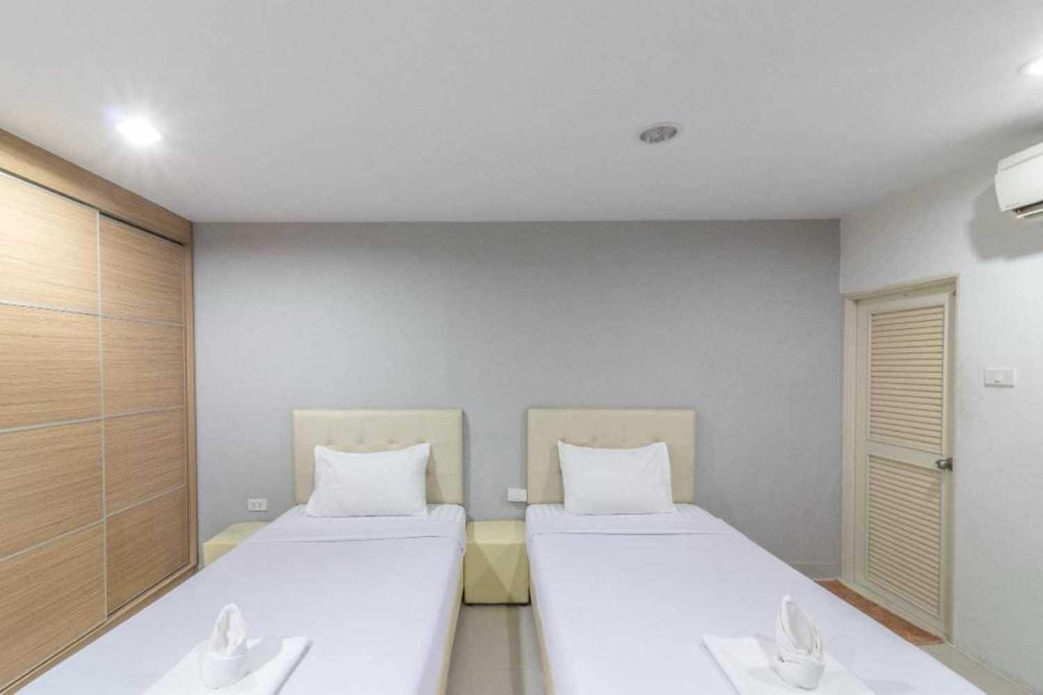 Habitación de hotel con dos camas individuales, un armario de madera, una pared blanca y una puerta con ventana.