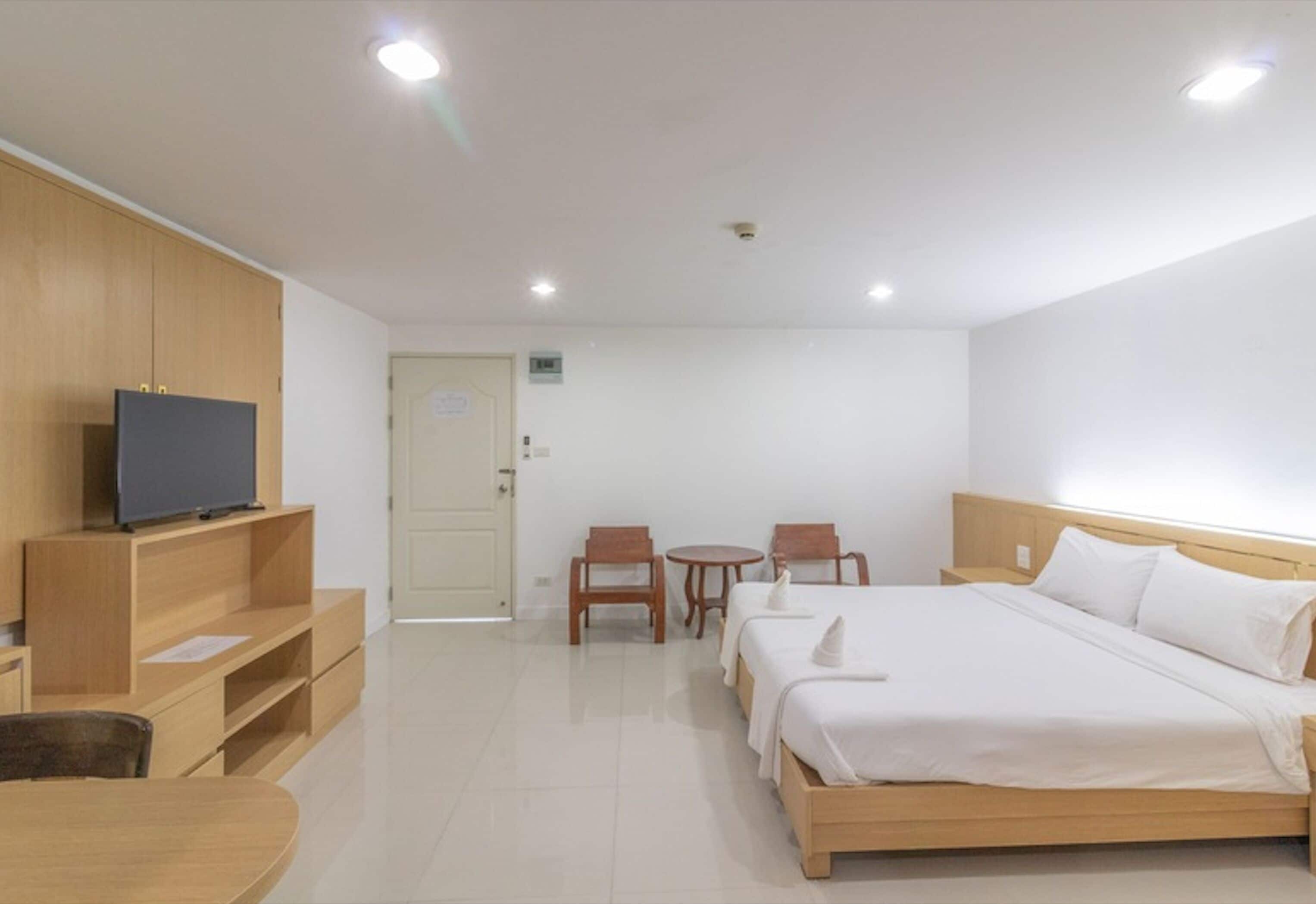 A hotel room with a bed, a TV on a wooden shelf, a desk, and two chairs.