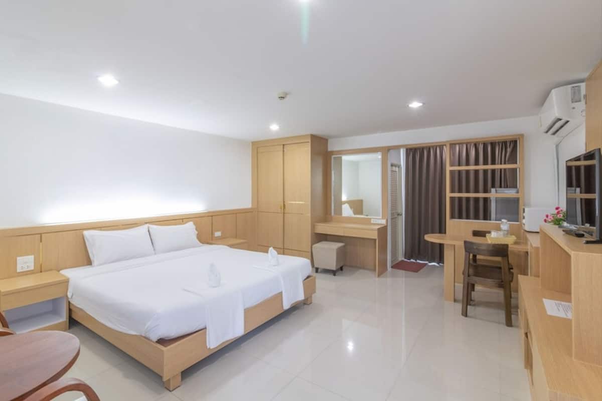 A hotel room with a bed, bedside table, desk, chair, and a small kitchenette area.